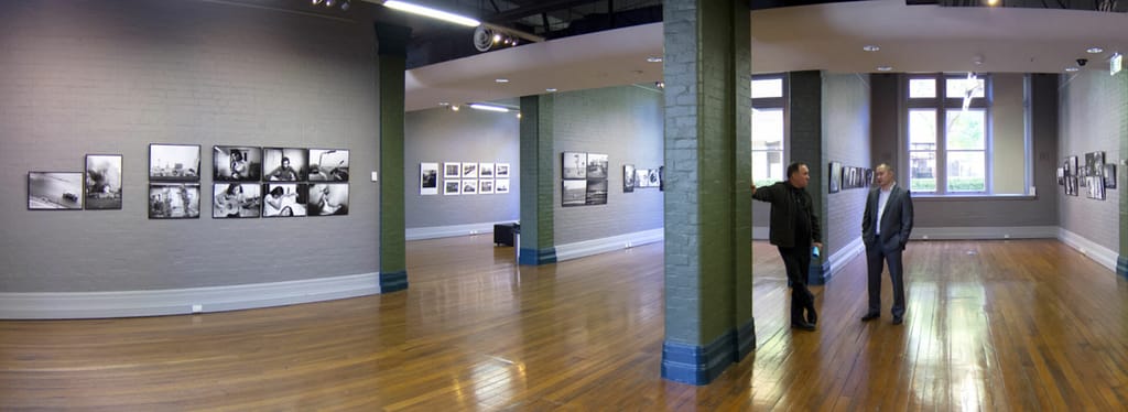 A group of people standing in a room at TAFE NSW Ultimo, admiring black and white photographs at The Muse.