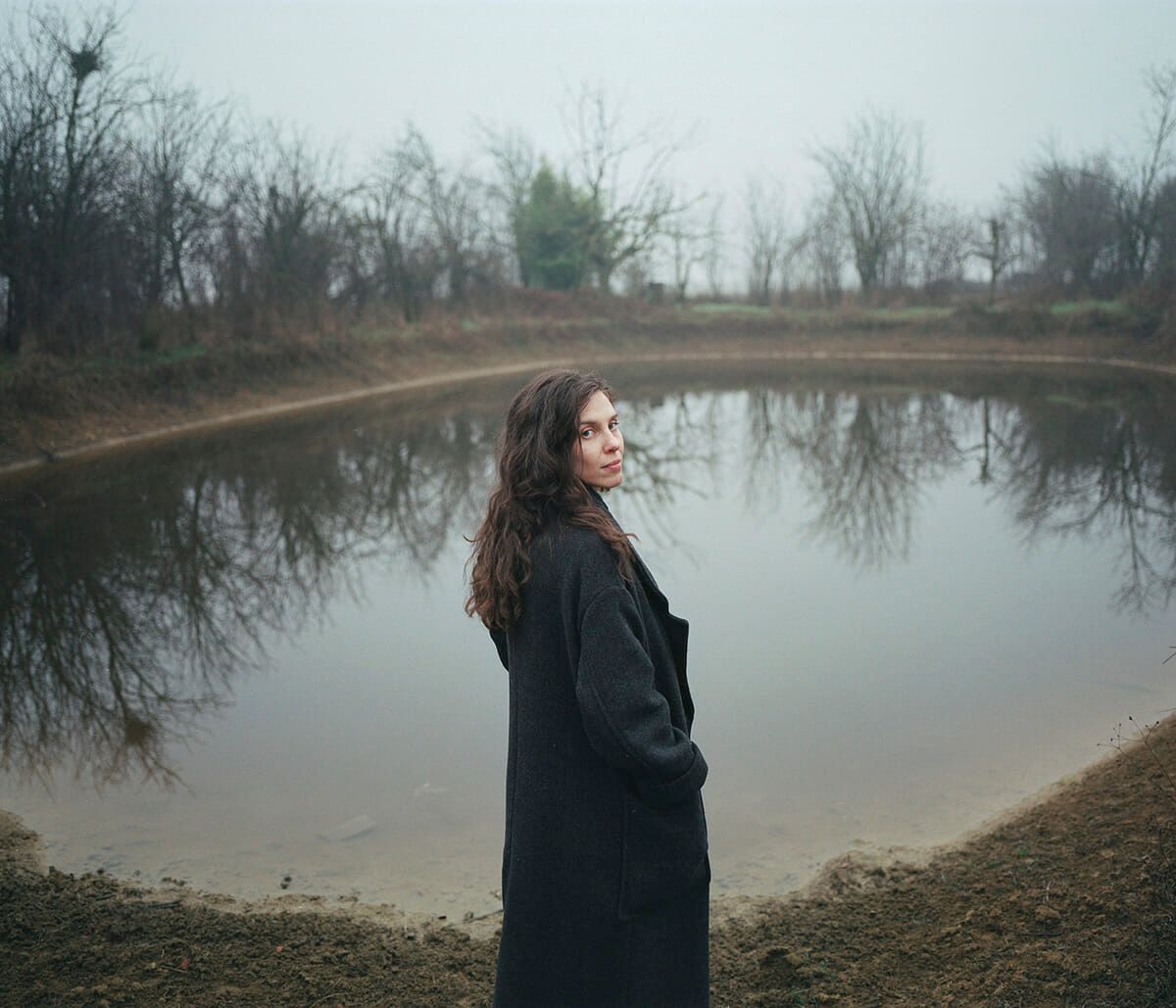 A woman is standing in front of a pond.