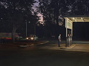 A man standing in front of a gas station at night.