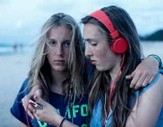 Two girls at the beach engaged in phone usage during the Head On Photo Festival.