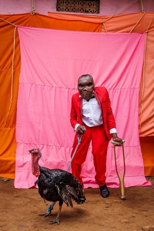 A man in a red suit walking a turkey, captured in a captivating Head On Portrait Awards 2023 submission.