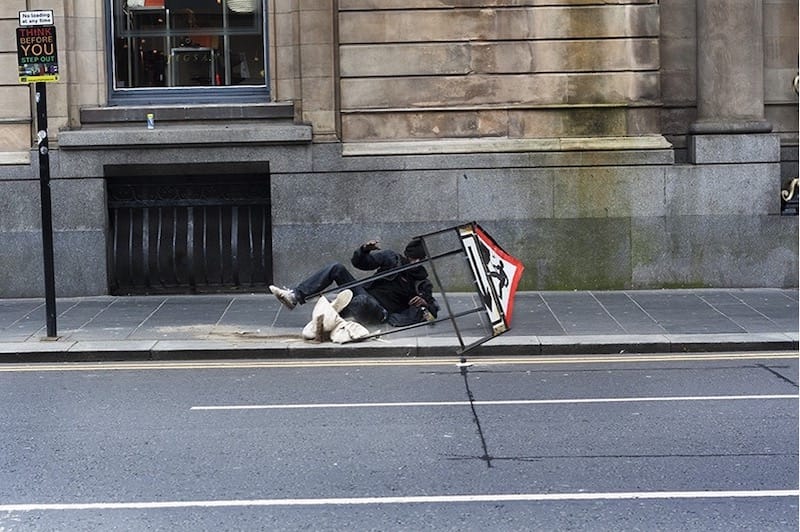 A man falls over a street sign