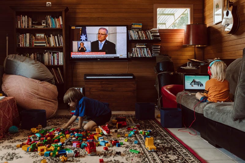 Children playing in their living room as the news of the Covid-19 outbreak plays on the television