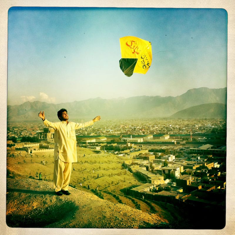 man standing on top of hill looking at kite