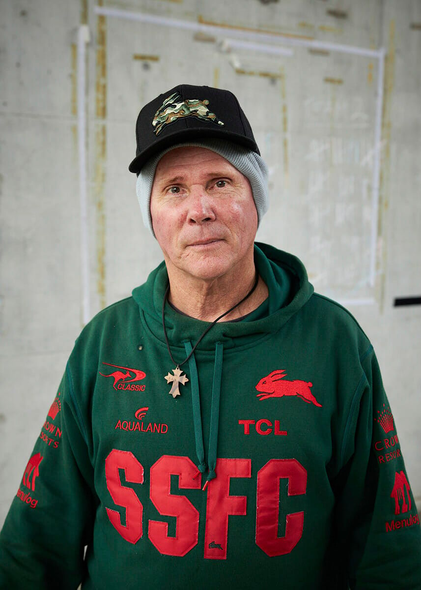 A man in a green hoodie standing in front of a wall.